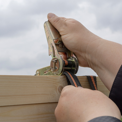 Hands using a ratchet strap to tie down lumber. 
