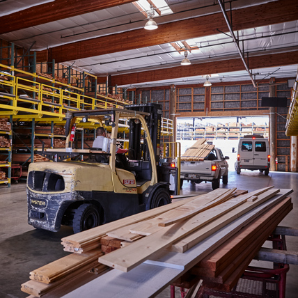 A line of two customer's vehicles and an employee operating a forklift, exiting the covered lumberyard with their lumber.