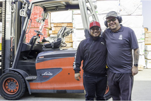Two Ganahl lumber employees smiling in front of a forklift. 